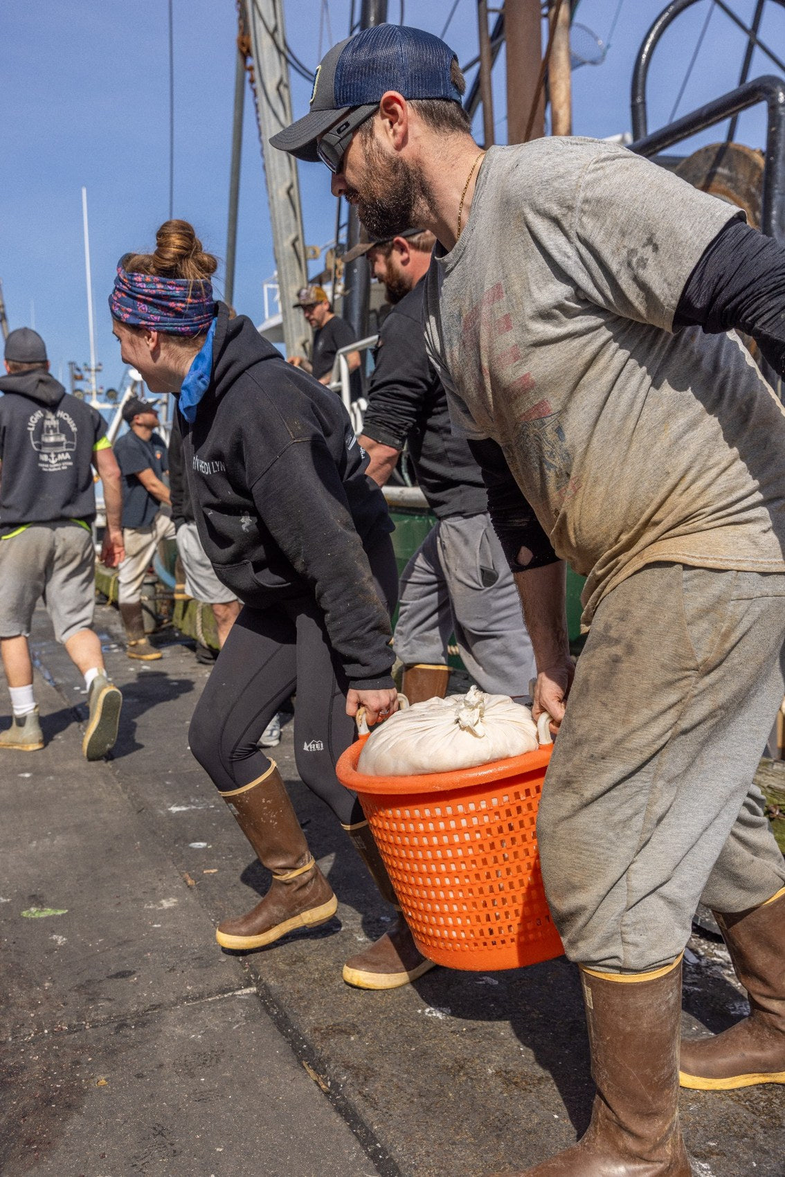 Working waterfront crew carrying a seafood basket beside a fishing boat