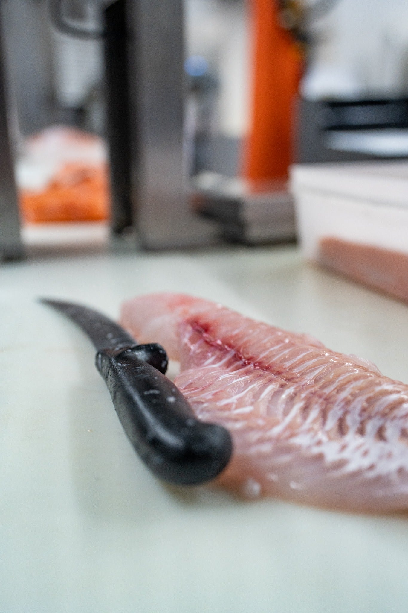 A seafood fillet with a fillet knife beside it on the cutting surface