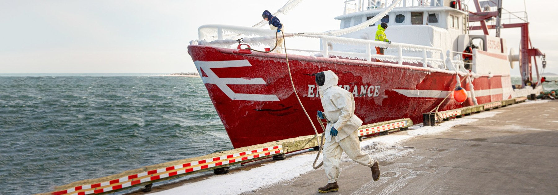 A dock worker handling a line beside an ice-covered red fishing boat